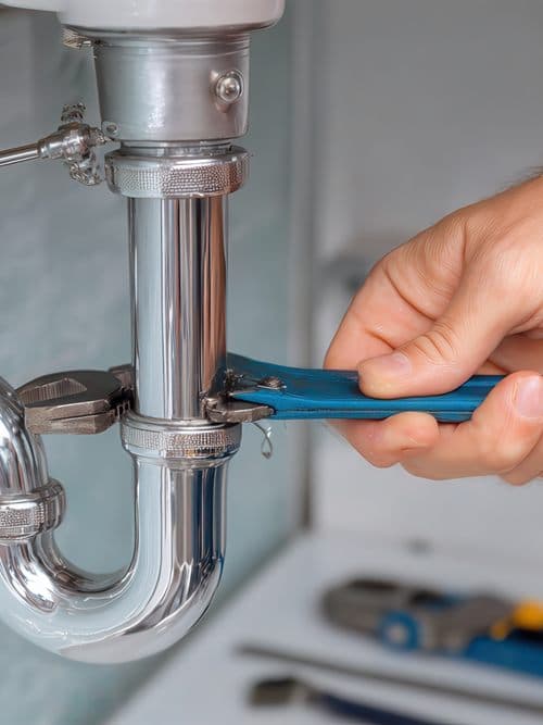 Fontanero apretando con llave inglesa el sifón de un lavabo durante un servicio de fontanería en Ourense